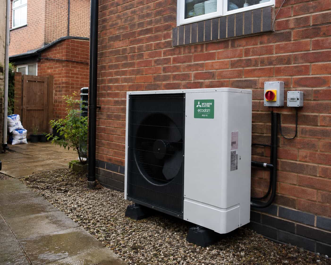 A modern domestic air source heat pump installed next to a brick house.