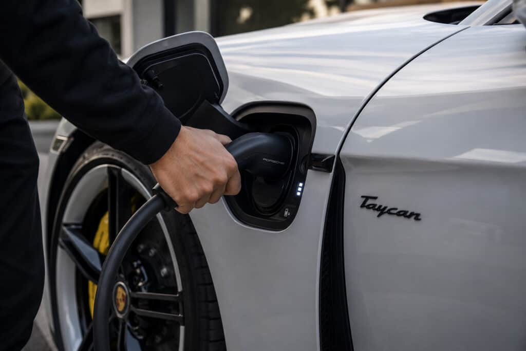 A person plugging an electric vehicle charging cable into a Porsche Taycan.