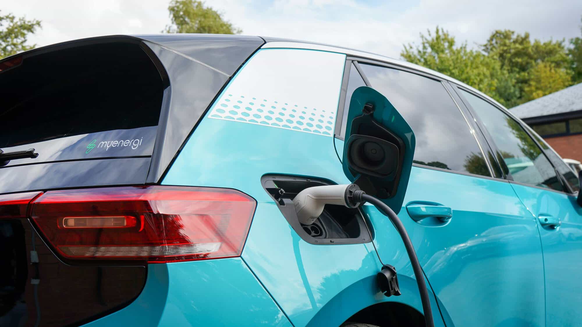 Side view of a blue Volkswagen ID3 electric vehicle plugged into a domestic charging cable.